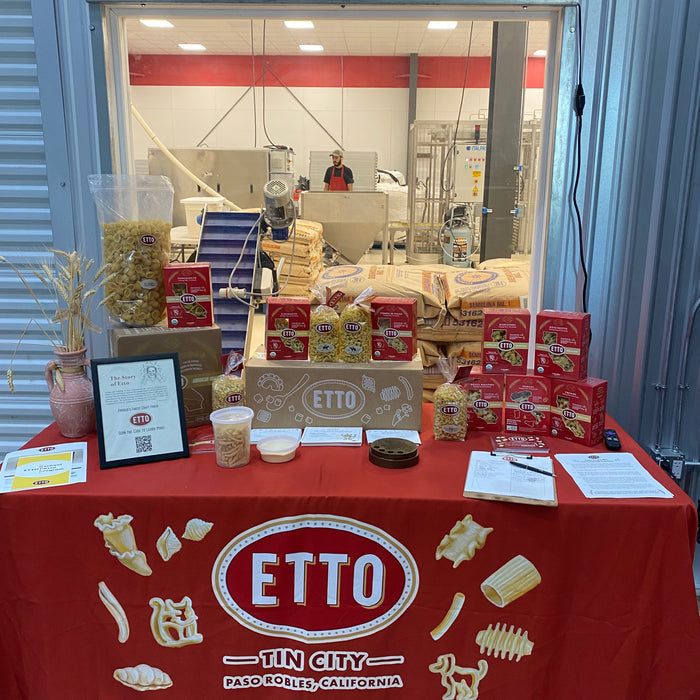 A display table at Etto Pasta Factory with various pasta shapes and packaging, with the Paso Robles, California backdrop.